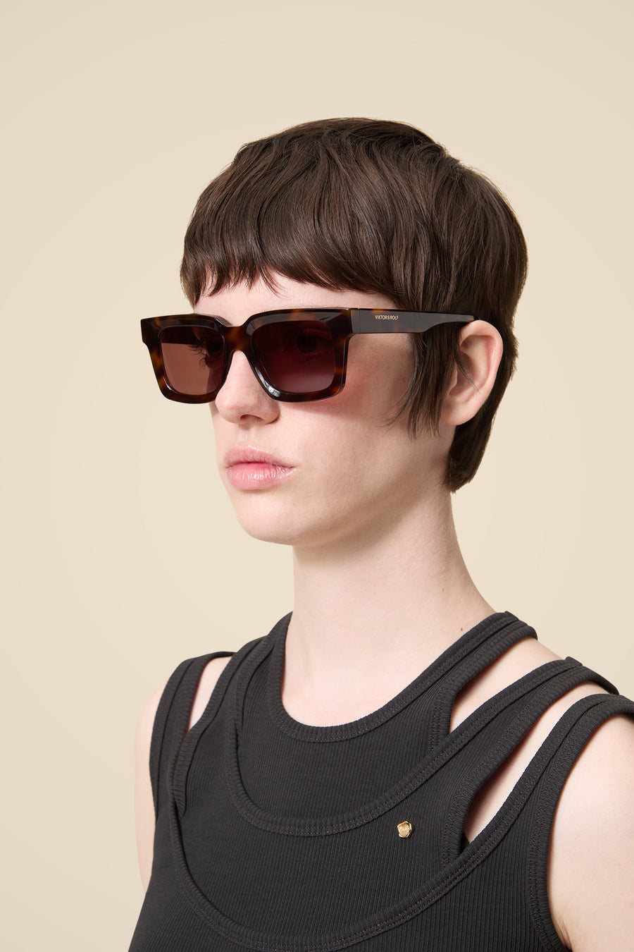 Stylish sunglasses with tortoiseshell frame, featuring square lenses. Model wears a black textured sleeveless top.