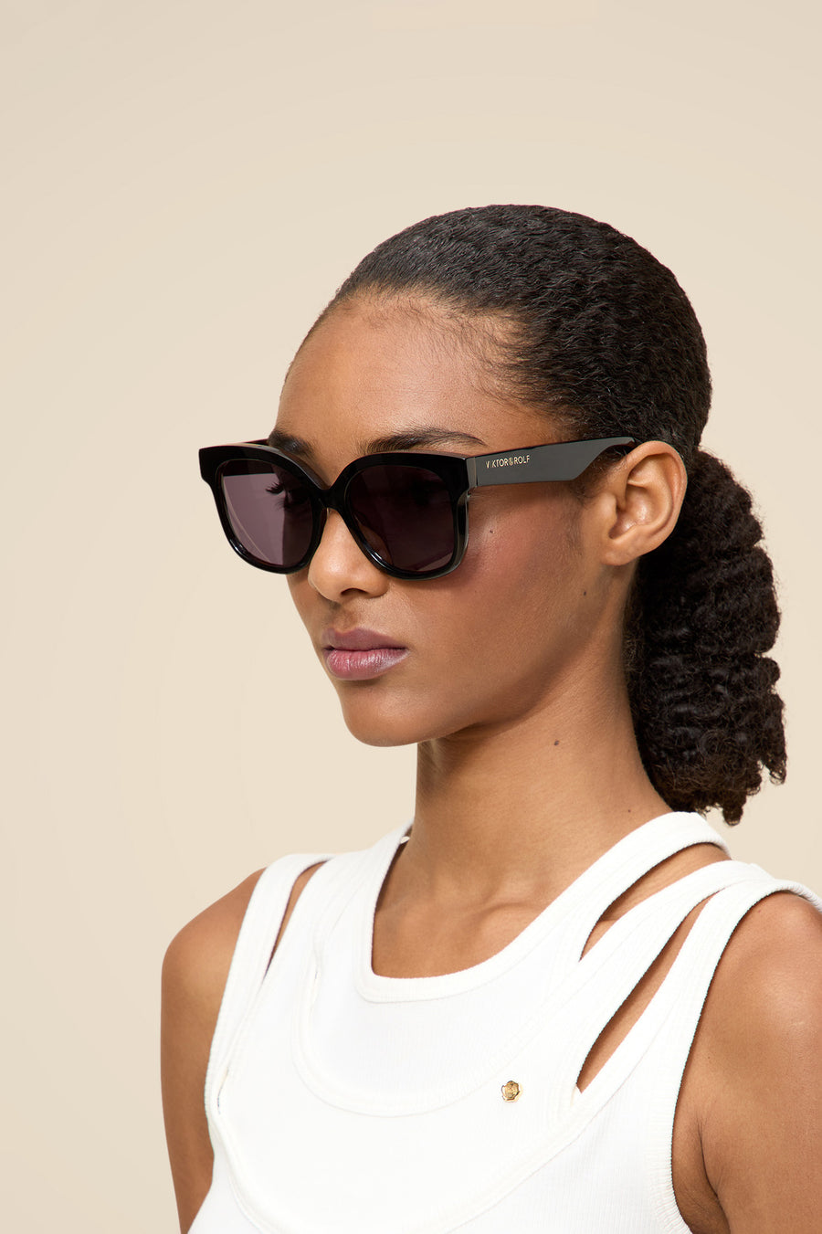 Stylish black acetate sunglasses with bold frames and tinted lenses, worn by a person in a chic white sleeveless top.