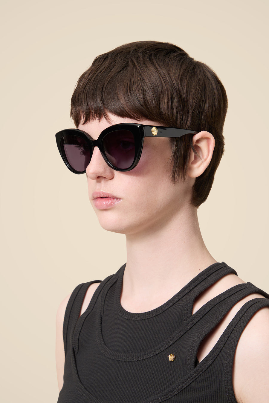 Stylish black sunglasses with large frames and a subtle gold emblem, paired with a sleeveless black textured top.