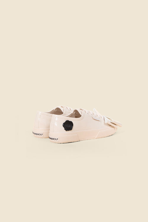 Beige patent leather sneakers with glossy finish, featuring black embossed logo detail and elegant ribbon laces.