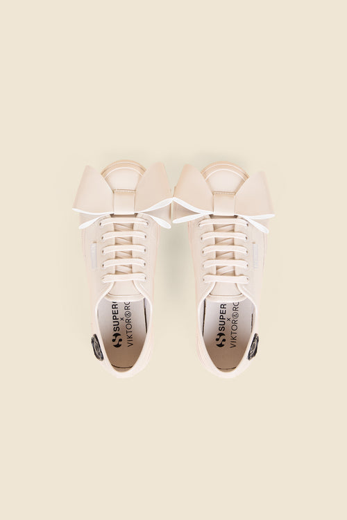 Cream sneakers with oversized beige bow detail, featuring tonal laces and subtle stitching on a light beige background.