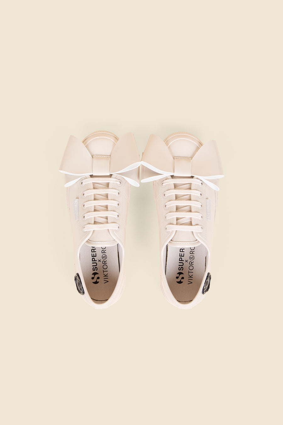 Cream sneakers with oversized beige bow detail, featuring tonal laces and subtle stitching on a light beige background.