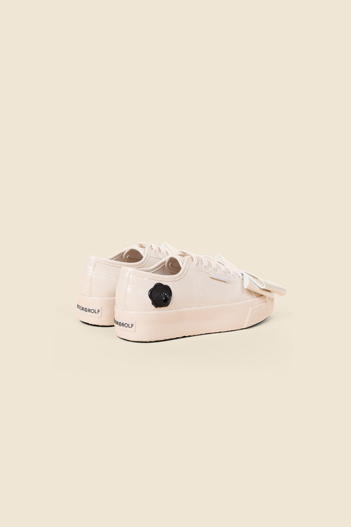 Cream patent leather sneakers featuring a sleek profile and black logo detail, creating a chic and modern look.