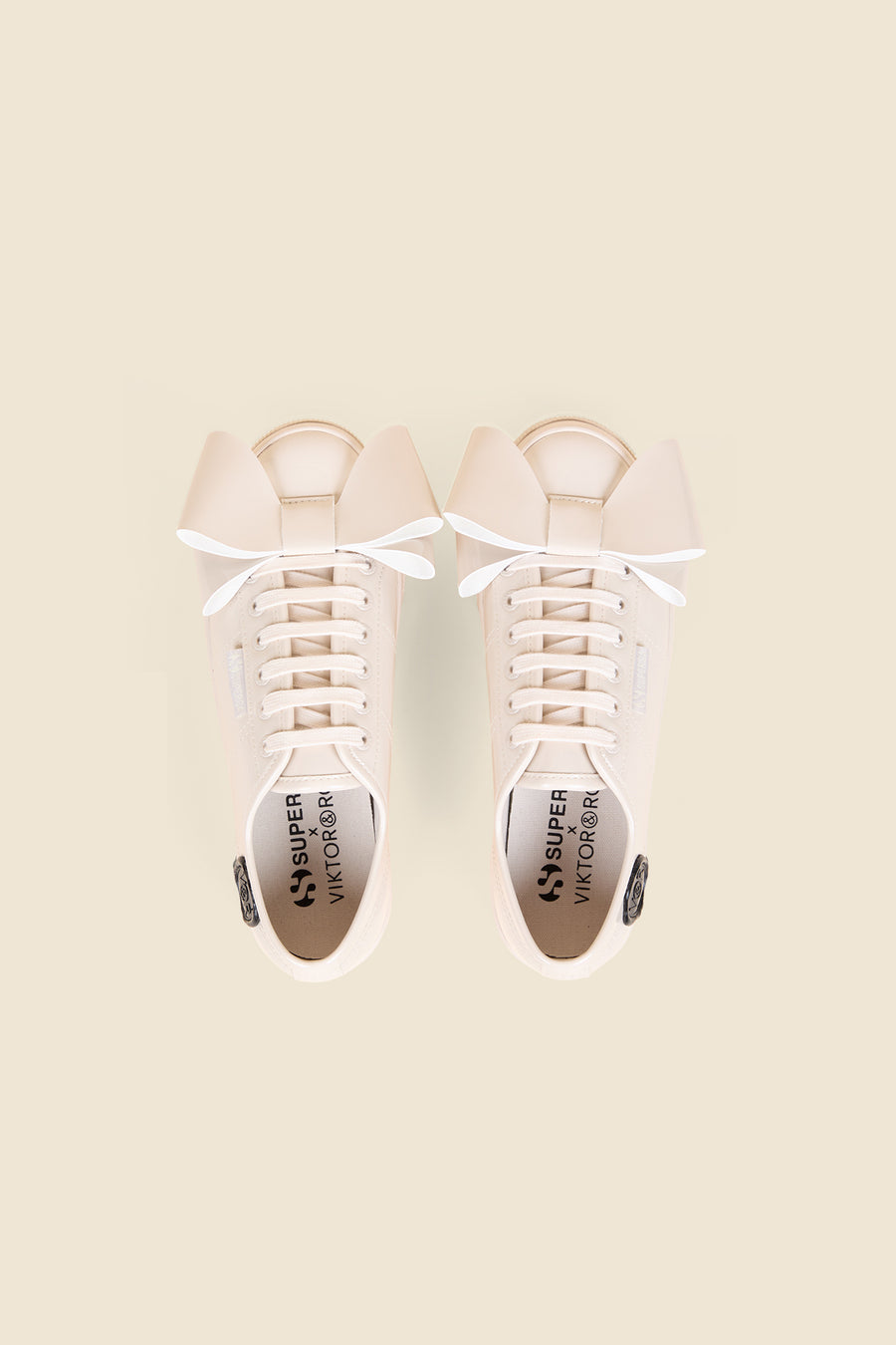 Cream sneakers with oversized bows on the tongue, featuring a collaboration logo on the insole and branded detailing.