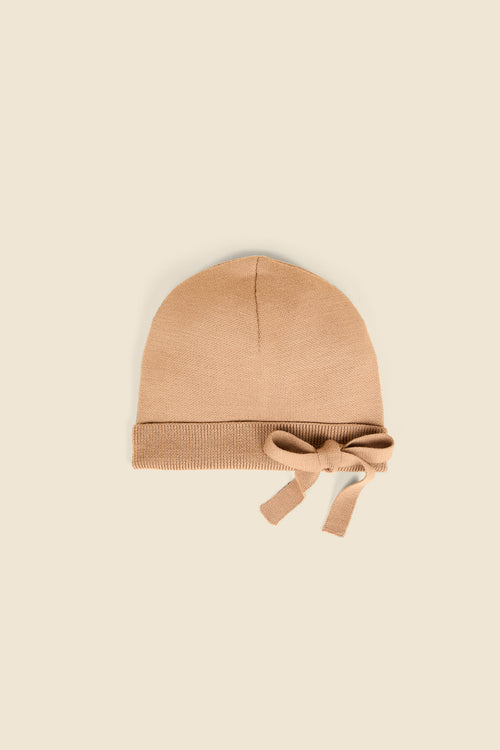 Cozy beige knit beanie with chic bow detail, providing a warm and stylish accessory for autumn and winter wardrobes.