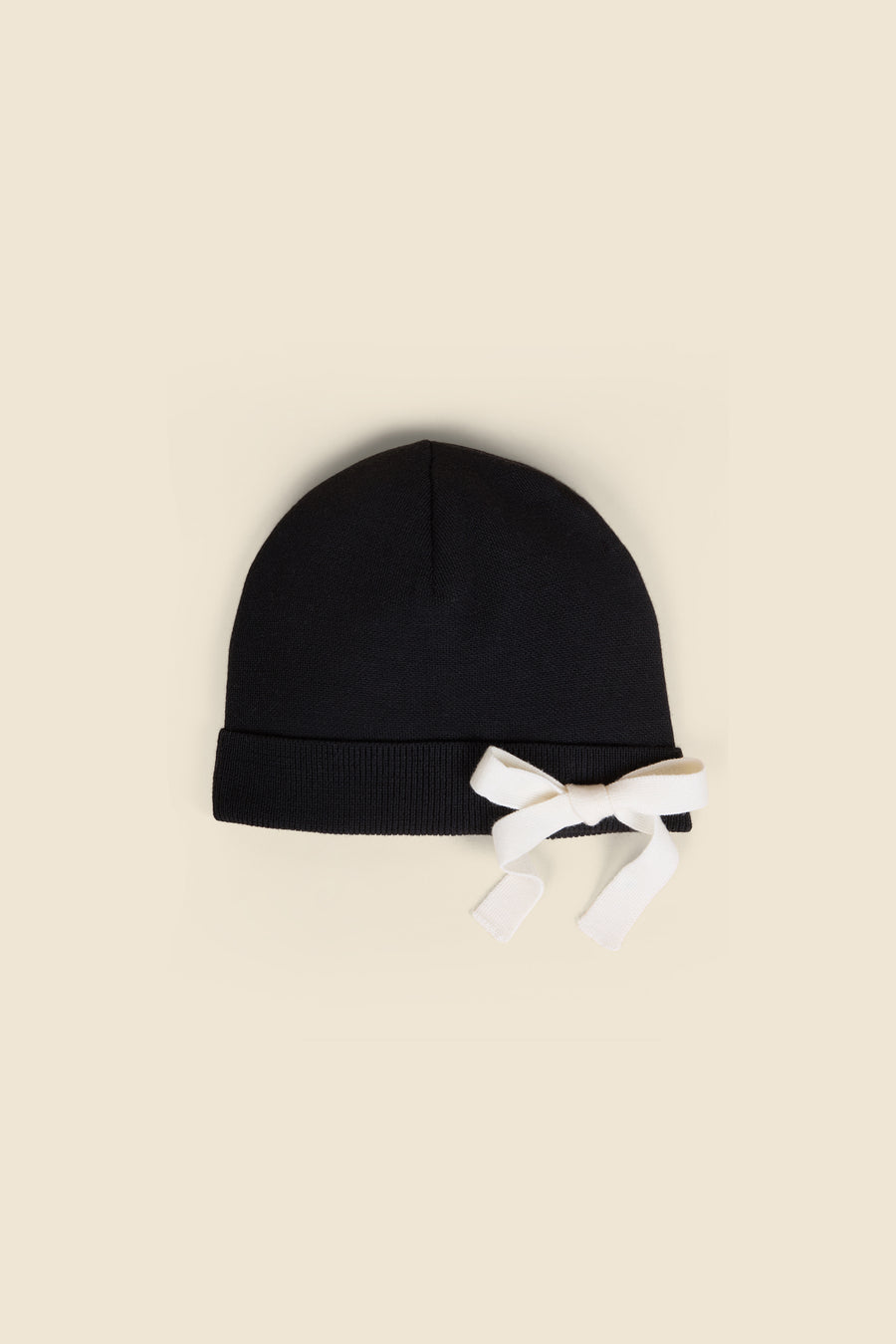 Black knitted hat featuring a ribbed cuff highlighted with a contrasting white bow, set against a plain backdrop.