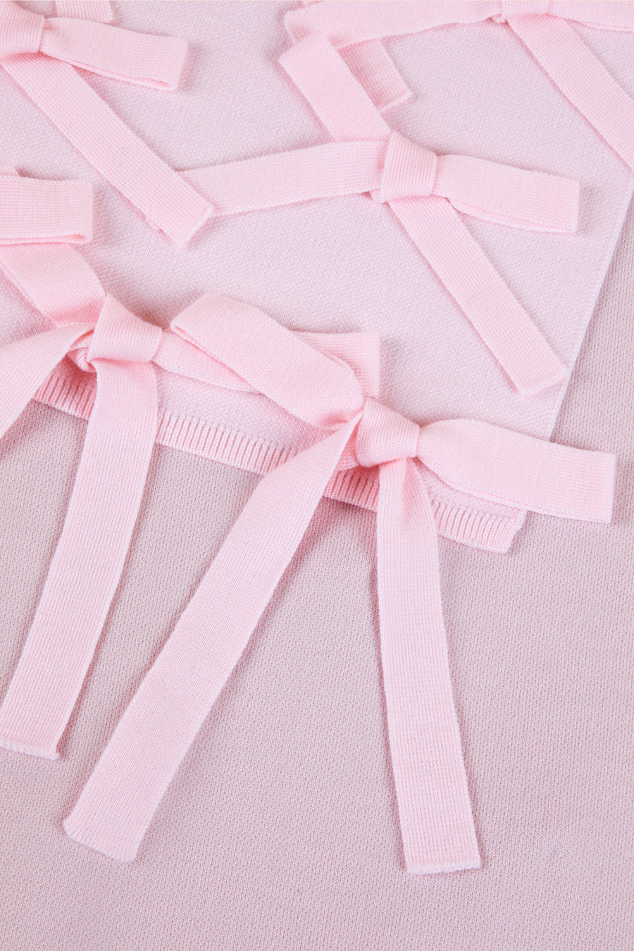 Soft pink knit fabric adorned with intricate bow details, showcasing delicate texture and pastel elegance.