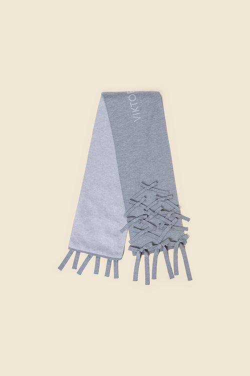 Elegant gray scarf featuring intricate fringe detailing and subtle logo design on a light and dark gray color block pattern.