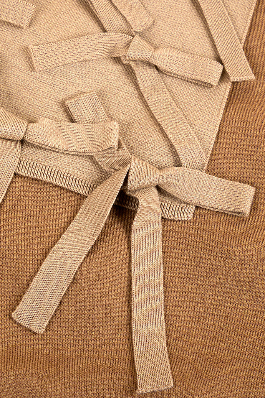 Knitted beige fabric with intricately tied bows and textured details, showcasing craftsmanship and design elegance.