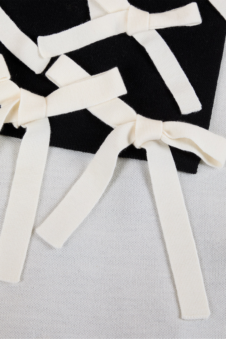 Cream knit bows intricately arranged on a textured black and white fabric, showcasing a striking contrast in design.