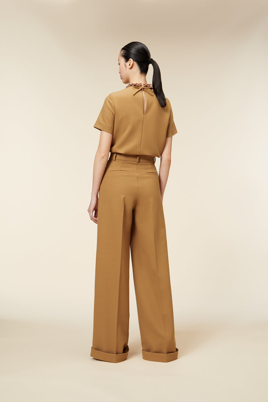 Tan tailored blouse and high-waisted pants with cuffed hems, featuring a knotted embellishment at the back neckline.