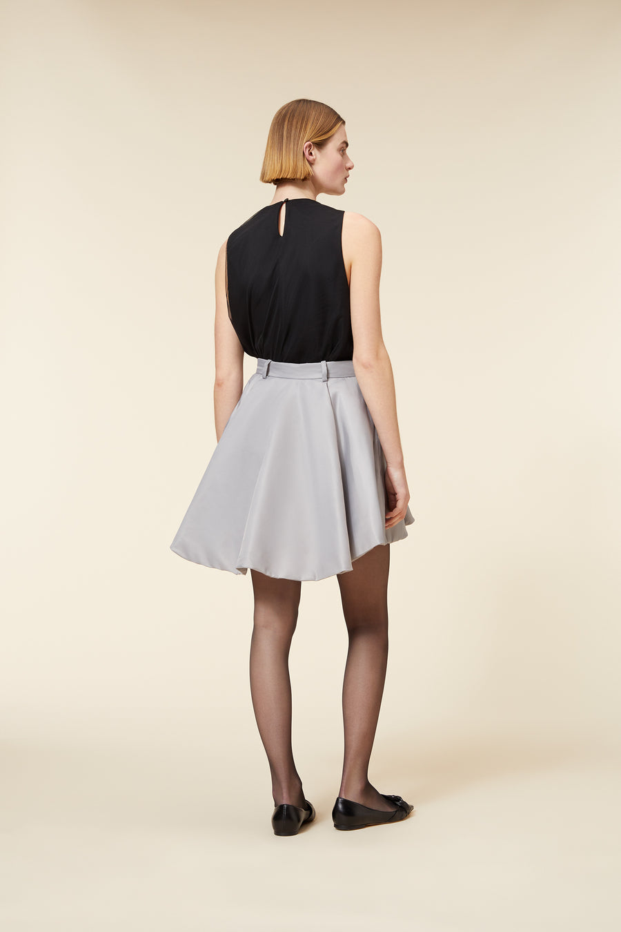 A-line skirt in soft gray fabric paired with a sleek black sleeveless top, captured in a minimalist studio setting.