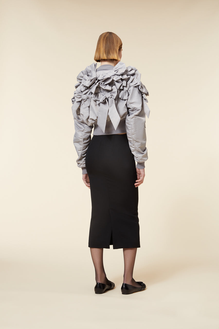 Elegant gray satin jacket with intricate bow detailing paired with a sleek black pencil skirt and black shoes.