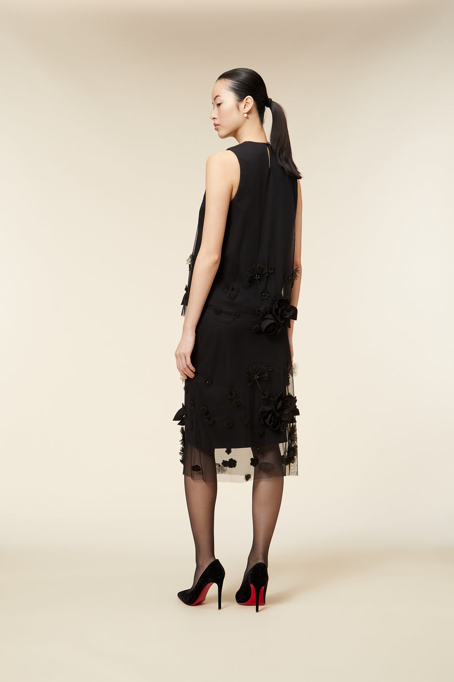 Elegant black sleeveless dress with floral applique details, paired with sheer stockings and black high heels.