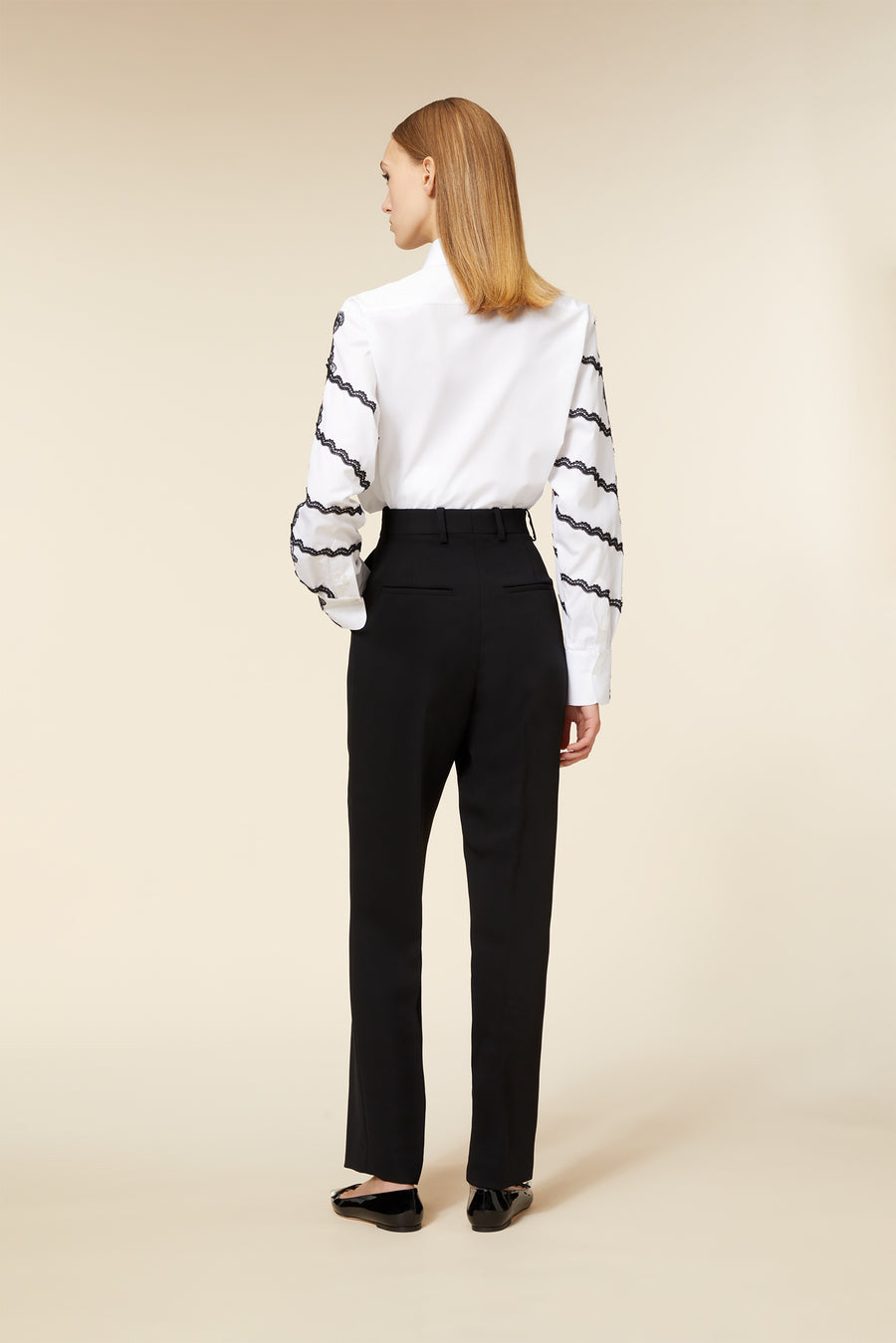 Elegant white blouse with black lace trim on sleeves paired with tailored black trousers, viewed from the back.