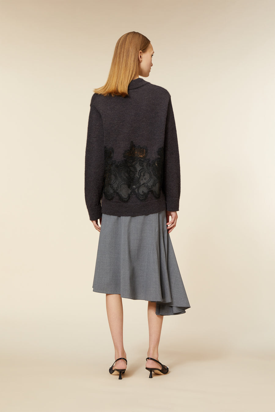 A charcoal wool sweater adorned with intricate lace detail, paired with an asymmetrical gray skirt and black sandals.