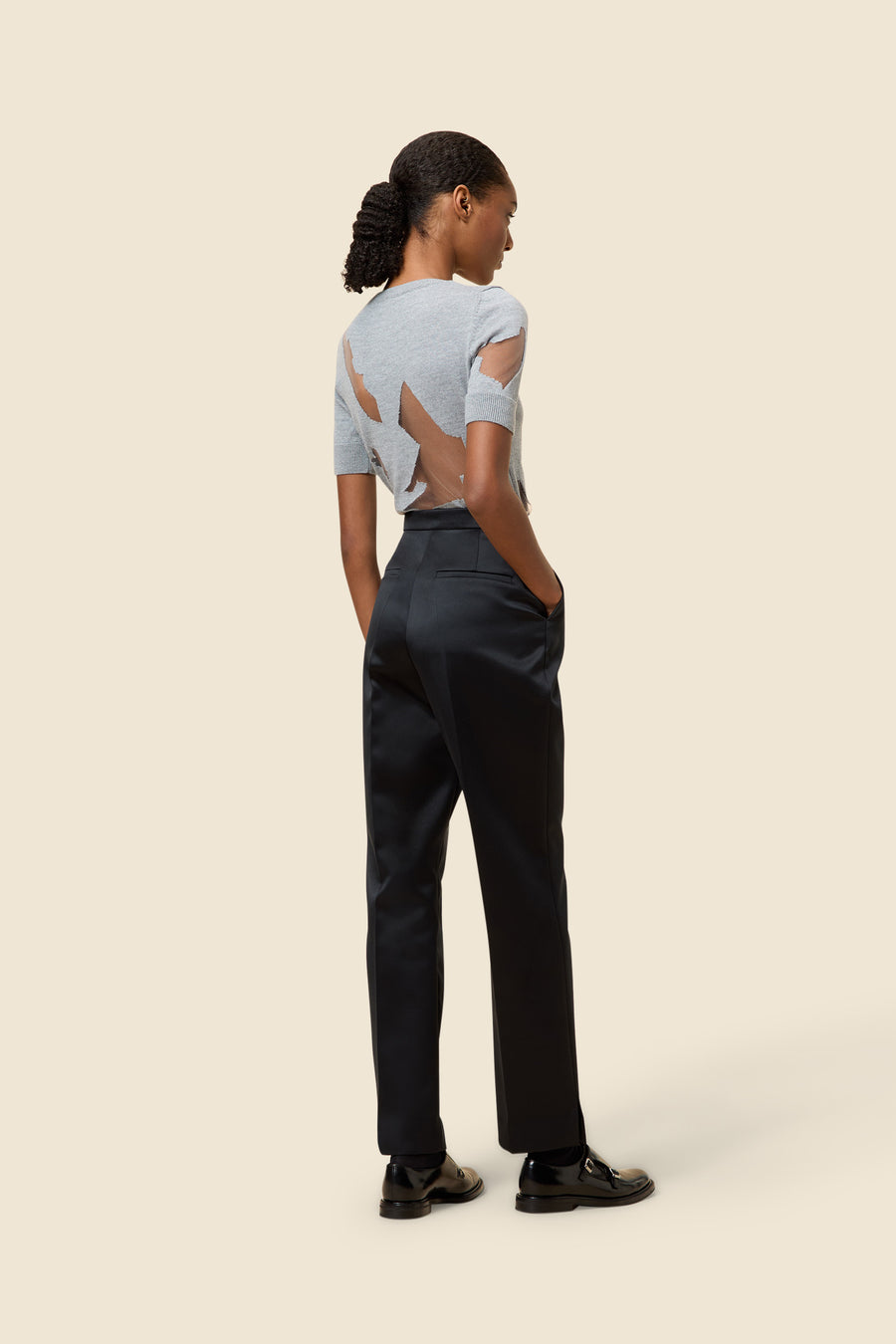 Elegant gray knit top with cutout patterns, paired with sleek high-waisted black trousers and stylish black loafers.