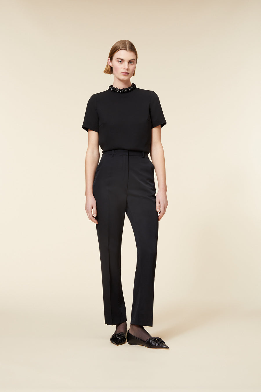 Elegant black outfit featuring a fitted short-sleeve top with beaded neckline, paired with high-waisted tailored trousers.