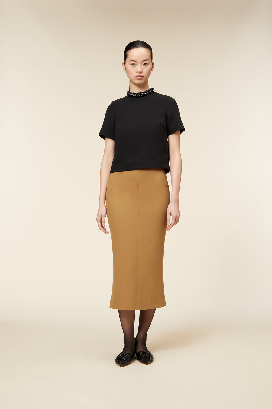 Elegant ensemble with a black high-neck top and a mustard pencil skirt, complemented by sleek black heeled shoes.