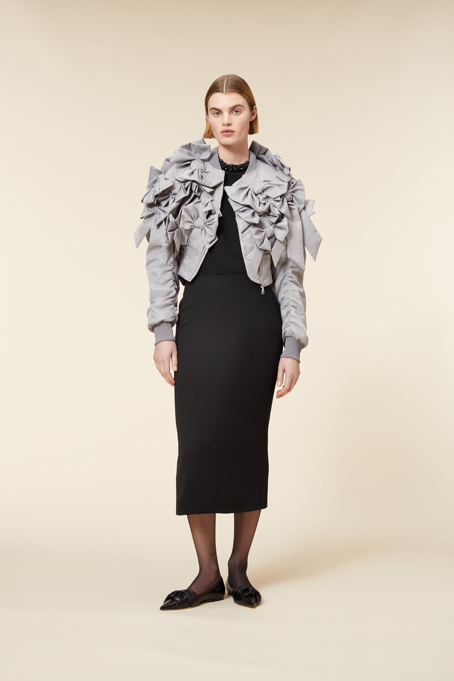 A tailored black dress paired with a statement gray jacket adorned with elaborate bow details and gathered sleeves.