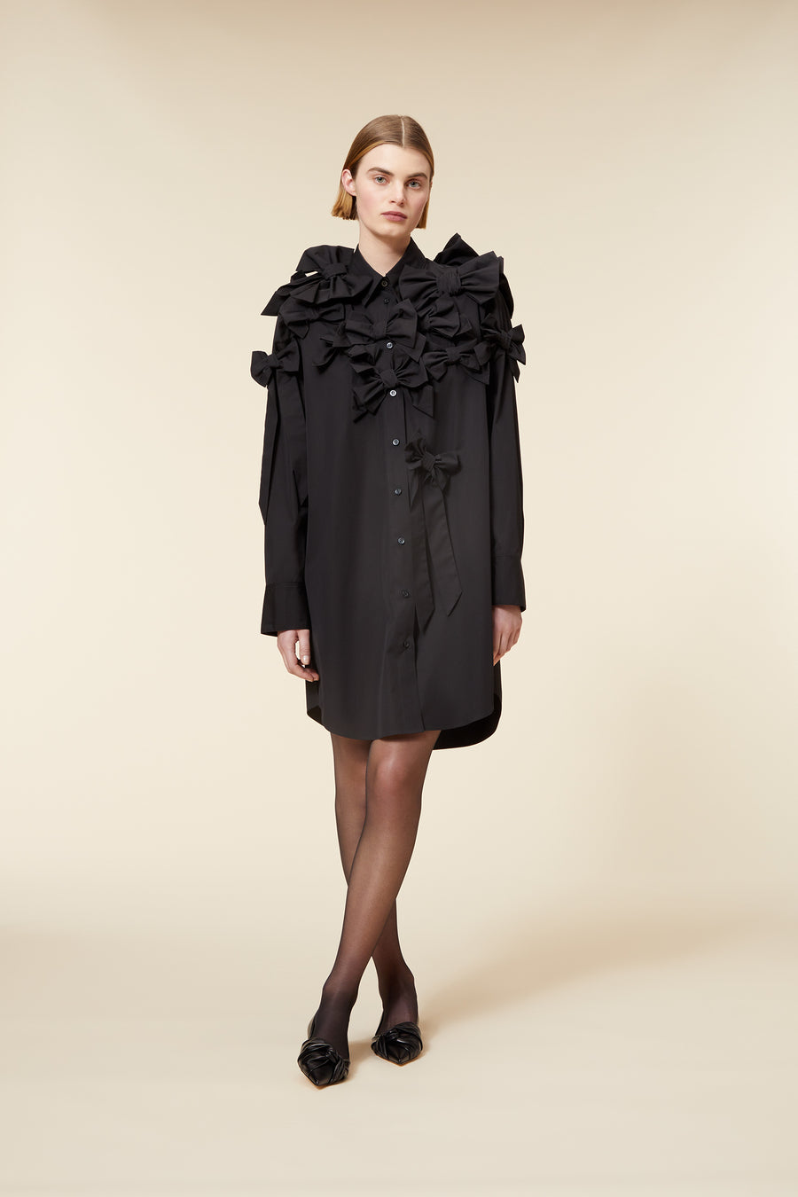 Black shirt dress with intricate ruffle and bow detailing, creating a sophisticated silhouette on a neutral background.