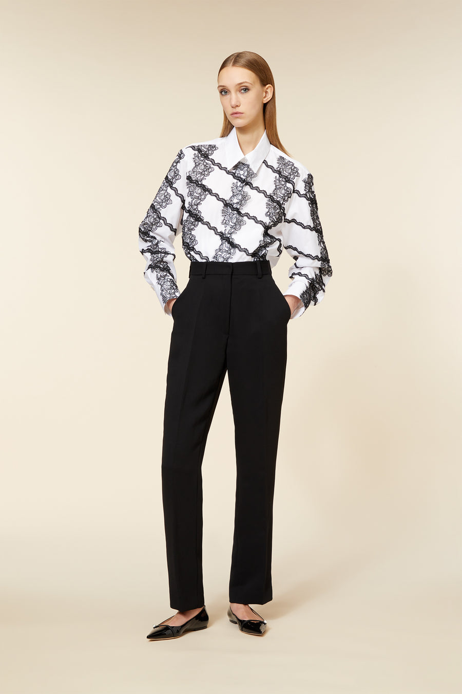 White blouse with black lace pattern paired with high-waisted black trousers, styled with sleek black pointed flats.