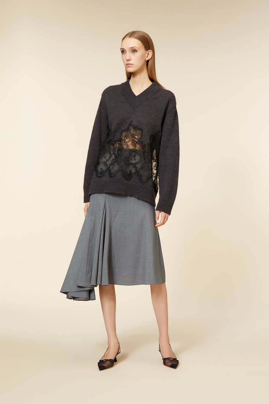 Model in a charcoal sweater with intricate black lace detailing, paired with an asymmetrical gray skirt and mesh flats.