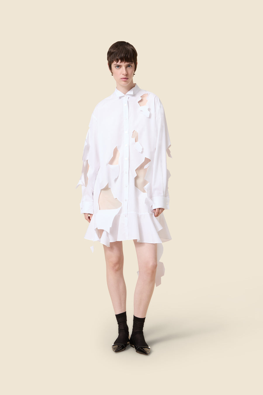 Innovative white shirt dress with artistic cut-out design, featuring a flared hem and classic collar on a minimalist backdrop.