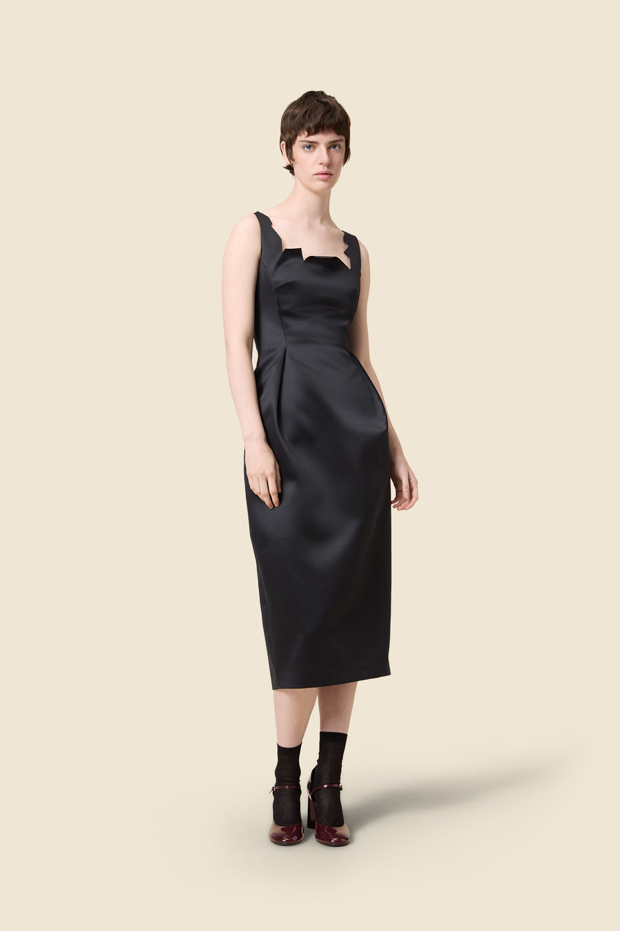 Sleek black satin dress featuring a bold geometric neckline and a fitted waist, highlighting a sophisticated style.