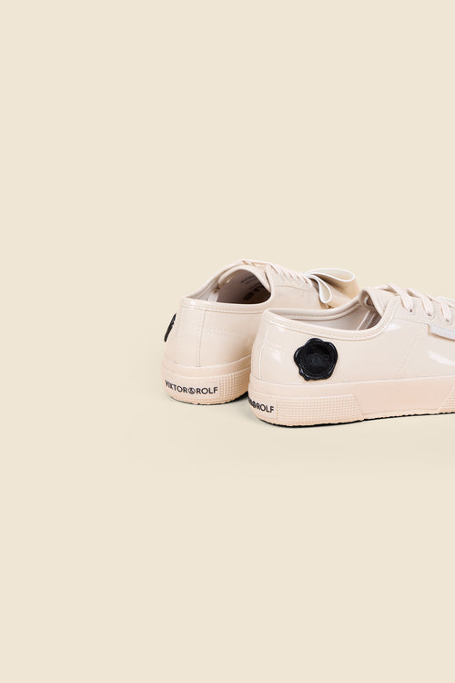 Elegant patent cream sneakers with black floral detailing, featuring logo branding on the heel against a neutral background.