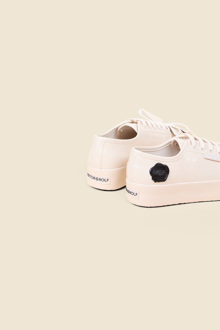 Cream patent leather sneakers featuring a minimalist design with embossed logo detailing on the heel and side patch.