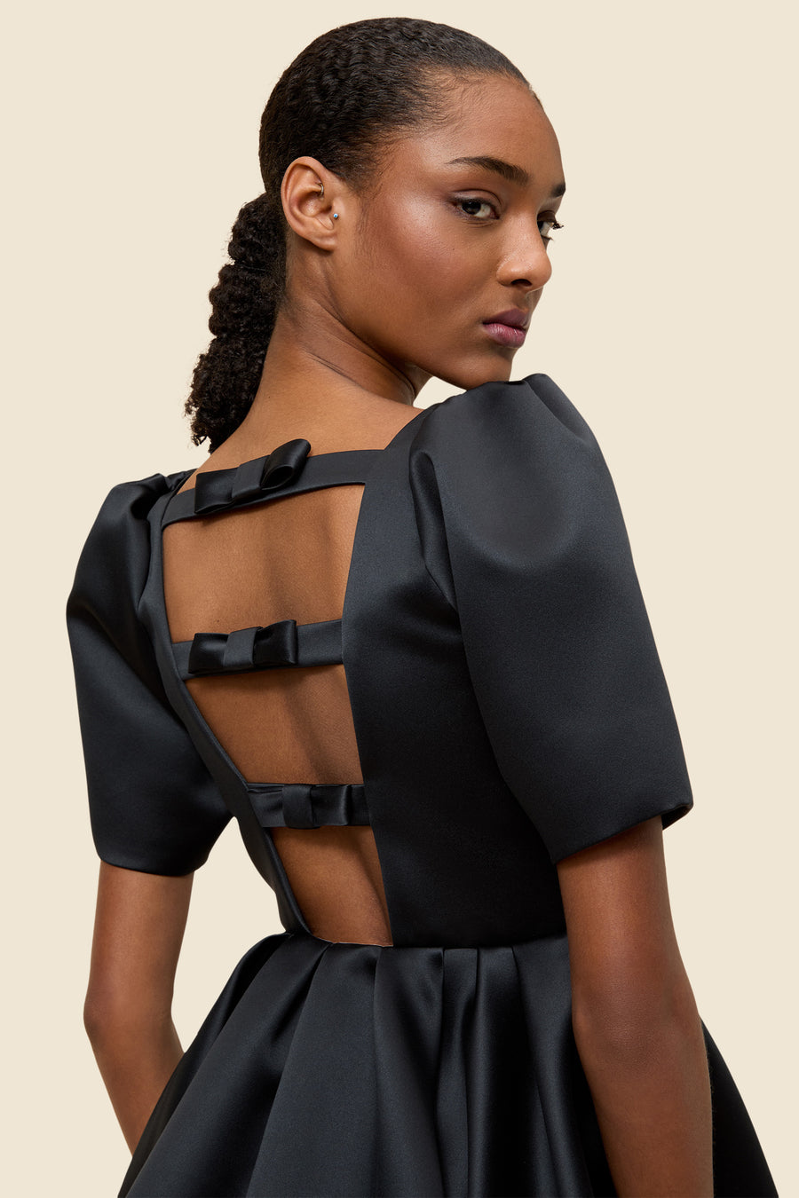 Elegant black satin dress with structured puff sleeves and three bow details on an open back design.