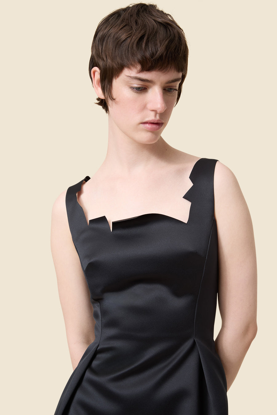 A sleek black satin dress featuring a unique angular neckline, elegantly tailored to highlight the shoulders.