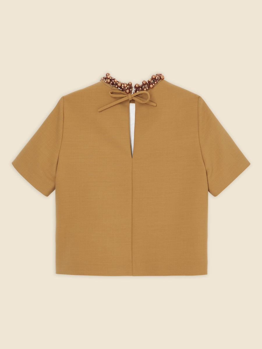 Tan-colored short-sleeve blouse with beaded neckline and back keyhole cutout, featuring a delicate bow tie closure.