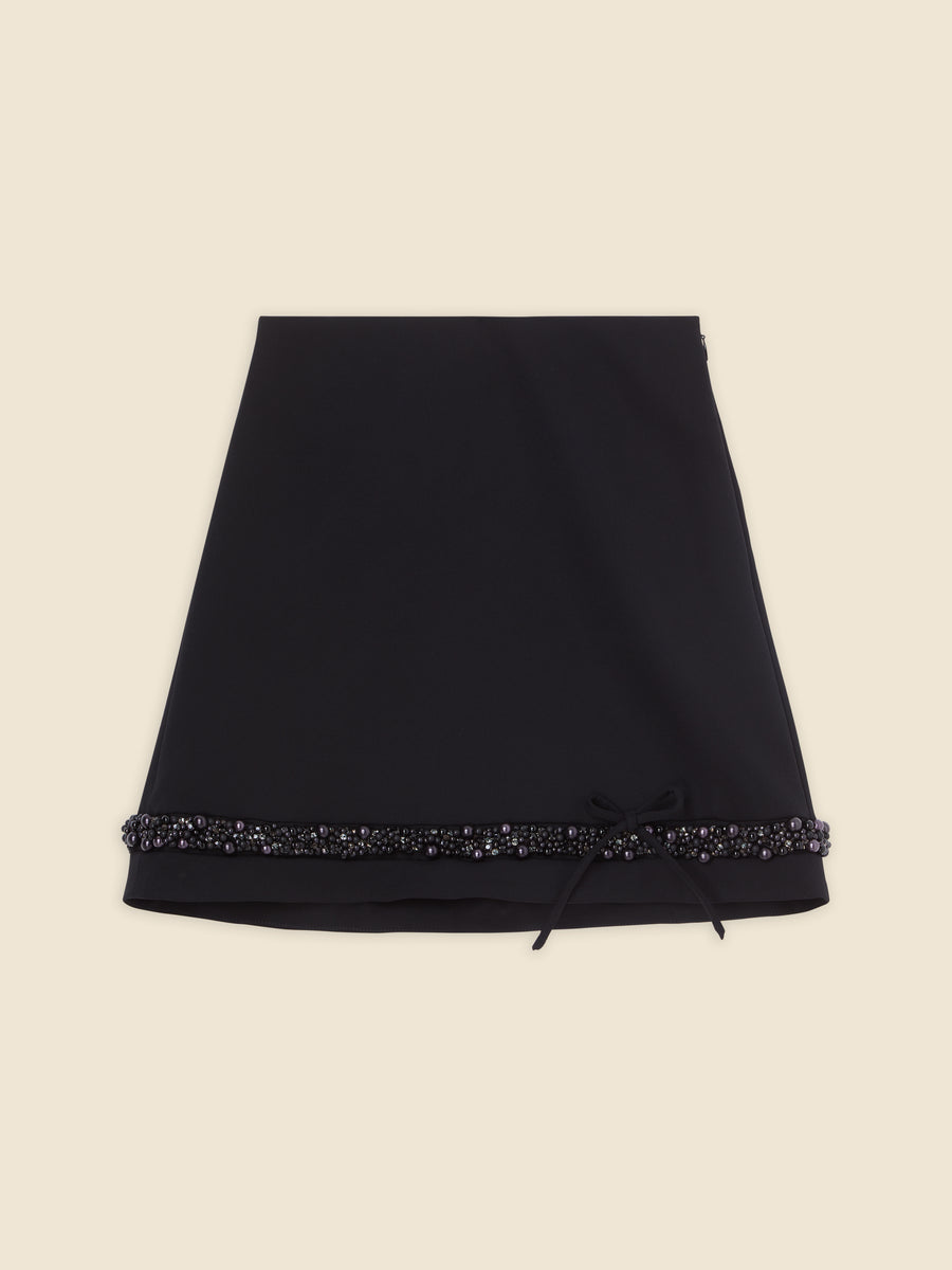 Elegant black skirt with intricate beadwork and pearl embellishments along the hemline, featuring a subtle side bow detail.