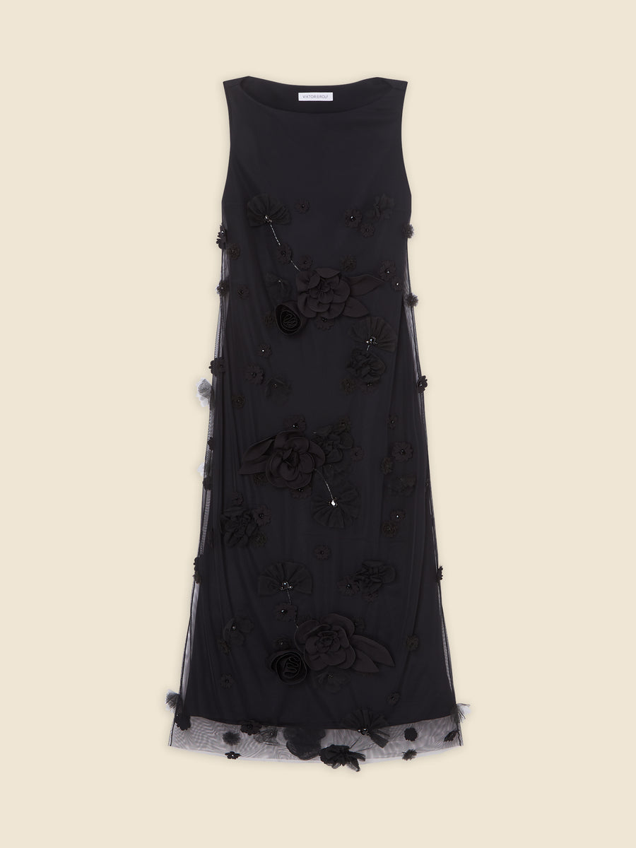 Sleeveless black floral evening dress with intricate floral applique and mesh detailing against a beige background.