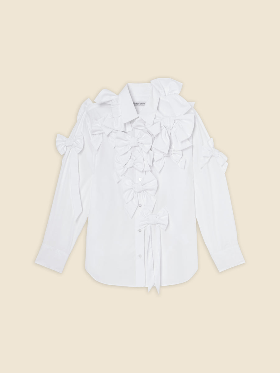 White cotton shirt with multiple decorative bows on the front and shoulders, featuring long sleeves and button-up design.