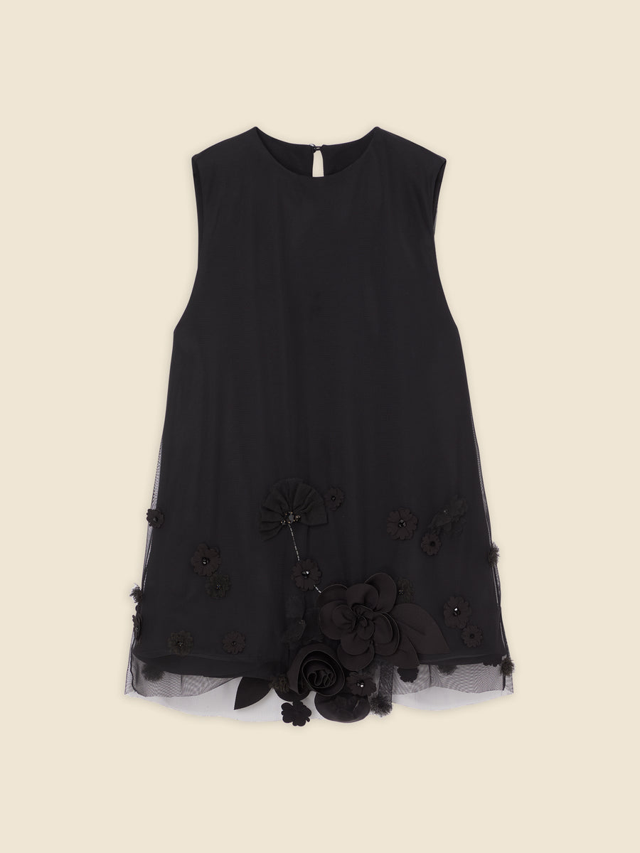 Black sleeveless dress with floral embellishments and layered textures over beige background, elegant and modern design.