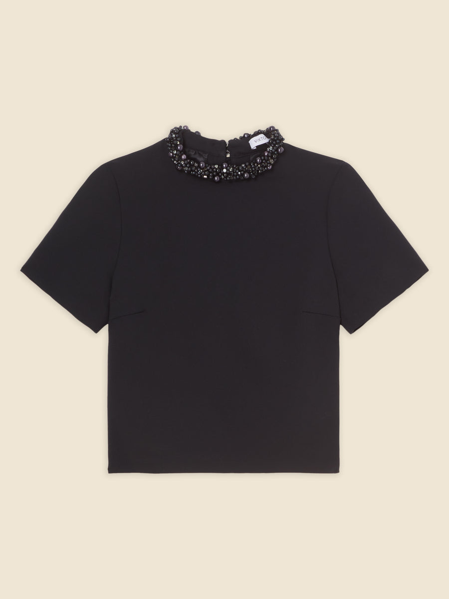 Black short-sleeve top with textured beaded neckline, elegant design on a cream background.